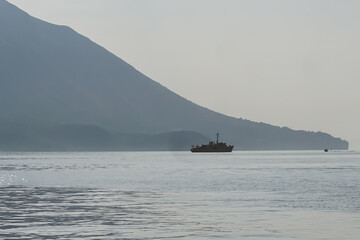 Scenic view of a ship sailing across calm waters with a hazy mountainous background, emphasizing...