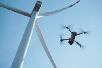 Drone hovering next to the blades of a wind turbine. The integration of modern technology in...