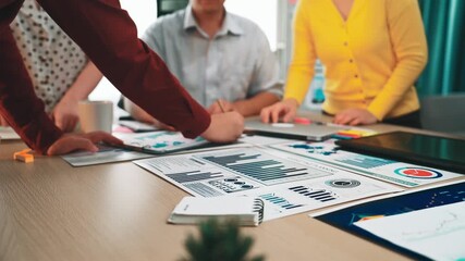 A diverse team of professionals engaged in a business meeting, analyzing charts and data on a table, emphasizing teamwork and strategic planning. SACTR - Powered by Adobe