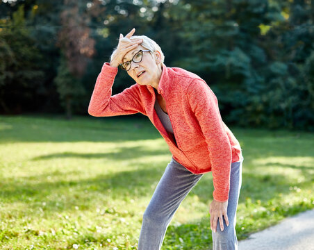 Portrait of a senior elderly woman exercising in a park, tired mature female running and taking a break outdoors, healthy lifestyle and cardio exercise in nature concepts, vitality and active senior