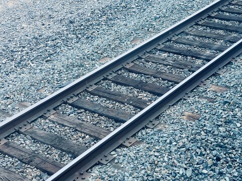 Close-up view of railway tracks showing detailed wooden crossties, steel rails, and crushed stone ballast with visible rail fasteners and hardware, cool coloring