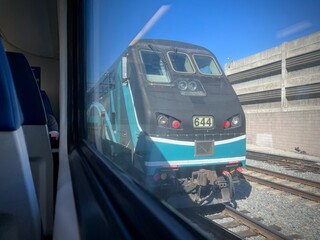 LOS ANGELES, CA, APR 19, 2025: view from inside a train showing Metrolink locomotive in teal and gray colors on parallel tracks, with concrete infrastructure and clear blue sky visible