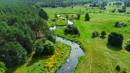 Aerial drone view of colorful kayaks floating along the winding Liswarta River, river surrounded by lush green meadows and summer nature landscape. Kayaking on river in Poland. Kayaks on a river