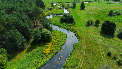 Aerial drone view of colorful kayaks floating along the winding Liswarta River, river surrounded by lush green meadows and summer nature landscape. Kayaking on river in Poland. Kayaks on a river