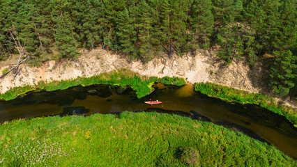 Aerial drone view of colorful kayaks floating along the winding Liswarta River, river surrounded by lush green meadows and summer nature landscape. Kayaking on river in Poland. Kayaks on a river