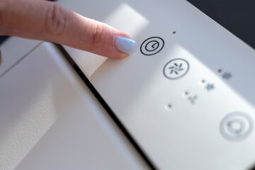 A close-up of a female hand with blue nail polish pressing a control button on a modern appliance.