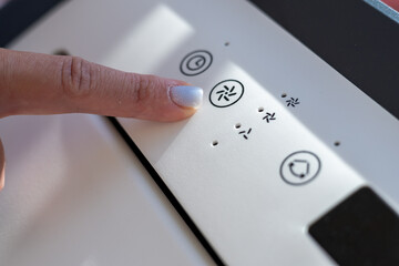 Close-up of a woman's hand with a light blue manicure, pressing a button on a white device.