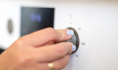 A close-up of a hand adjusting the temperature dial on an oven, showcasing pastel blue nails and a modern kitchen setting.