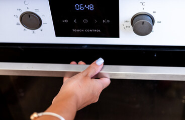 A close-up of a hand adjusting the oven settings, highlighting modern touch control features in a...