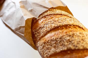 Freshly baked bread with sesame seeds peeking out of a brown paper bag, highlighting its crispy crust and golden hue.