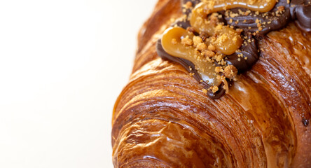 Close-up of a decadent croissant topped with chocolate, caramel sauce, and crushed nuts.