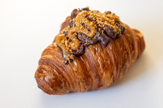 A delicious croissant topped with chocolate ganache and drizzled with caramel, creating a tempting treat for pastry lovers.