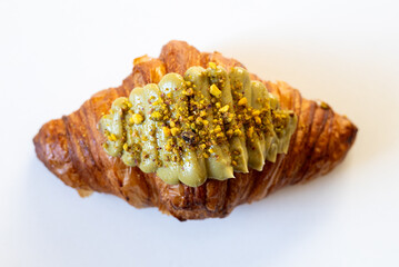 A delicious croissant topped with vibrant green pistachio cream and crushed pistachios, showcasing gourmet pastry artistry.