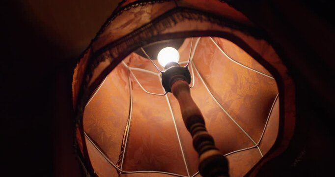 An old floor lamp with a fringe shines in the dark bottom view