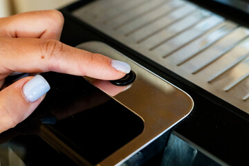 A close-up of a woman’s hand with light blue nails pressing the button on a coffee machine,...