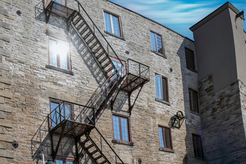Exterior of four storey old brick and stone building, casement windows, sun flare in window, black...