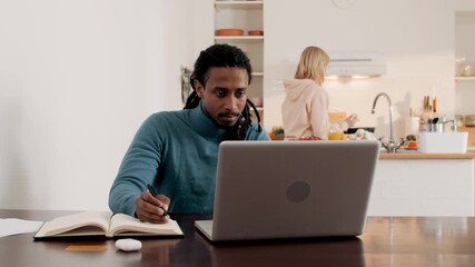 Focused man working from home while woman prepares meal