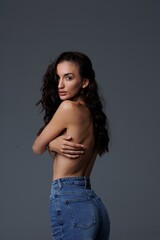 Beautiful tall thin brunette with curly hair in the studio, cyclorama. The girl stands shirtless...
