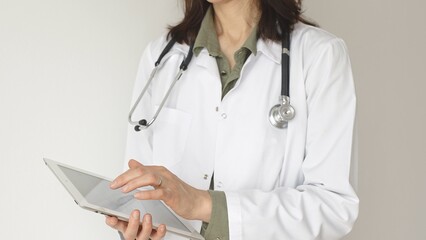 Close up of woman doctor, wearing white coat over a green blouse and a stethoscope, is using a...