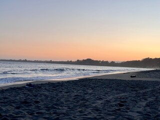 A peaceful ocean sunset with gentle waves washing onto the sandy beach, creating a reflective glow of orange and purple hues