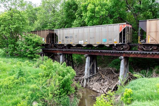 Fototapeta Railroad freight cars on wooden trestle in Cloud County, Kansas. Steam running underneath the bridge. Green grass in foreground, trees in background.  