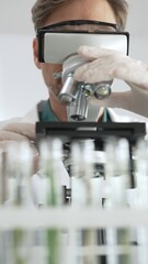 Man scientific researcher in protective gear analyzing specimens through a microscope in a sterile laboratory environment. Medicine, health care and science concept
