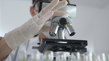 Scientist wearing white gloves adjusting microscope in laboratory setting, conducting scientific research surrounded by test tubes. Medicine, healthcare and science concept