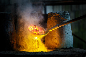 blacksmith holding a hot crucible by the iron pliers from furnace and pouring the melting gold into...