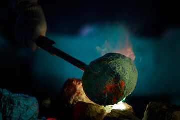 blacksmith holding a hot crucible by the iron pliers from furnace and pouring the melting gold into...