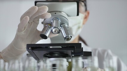 Scientist wearing white gloves adjusting microscope in laboratory setting, conducting scientific...