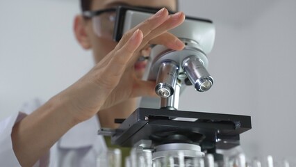 Female scientist analyzing test samples under microscope in contemporary research environment of...