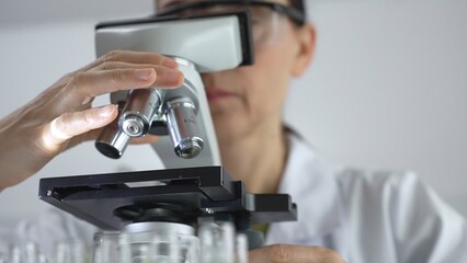 Female scientist analyzing test samples under microscope in contemporary research environment of laboratory. Medicine, healthcare and science concept