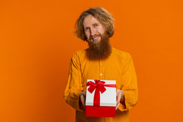 Positive smiling Caucasian man presenting birthday gift box stretches out hands offer wrapped...