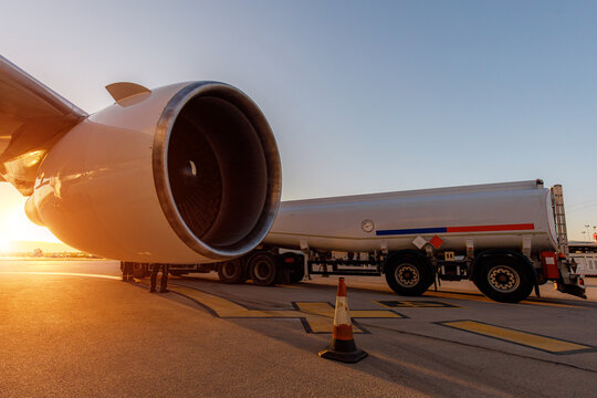 Aircraft fueling process at sunset with a close-up view of a jet engine and fuel truck