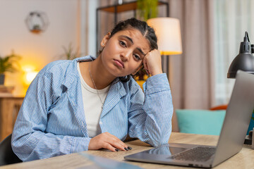 Sad Indian woman looks pensive thinks over life concerns or unrequited love, suffers from unfair situation. Problem, break up, depressed feeling bad, burnout. Girl at home office at table. Lifestyle.