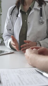 Doctor woman is explaining diagnosis to male patient during a medical consultation in a medical office, gesturing with hands, vertical close up view. Medicine and health care concept