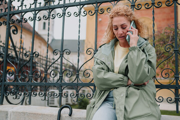 Woman leaning on a fence making a phone call on a cloudy day