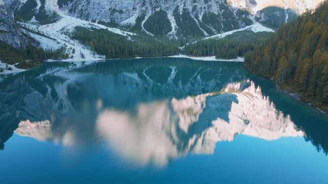 Pristine mountain lake reflecting snow capped peaks and drifting clouds at Lago di Braies, showcasing breathtaking alpine landscape in Dolomites, Italy