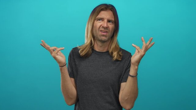 Man with long blond hair making finger quotes gesture with both hands and a skeptical expression in a studio; skepticism humor.