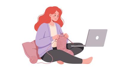 A smiling red-haired woman in a purple cardigan knitting with pink yarn while watching a tutorial on her laptop.