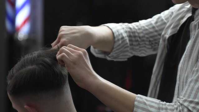Professional barber carefully combing client's hair, preparing precise hairstyle with expert grooming techniques in modern barbershop setting