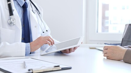 Close-up of doctor man showing information on tablet to patient woman during medical visit, explaining diagnosis and treatment options, providing medical consultation. Medicine concept