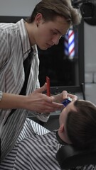 Professional barber trimming customer's hair with electric clipper, focusing on precise nape...