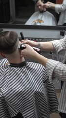 Professional barber grooming client's hair using electric clipper, delivering precise cut with...