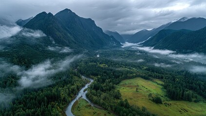 Aerial view of a misty valley, a meandering river flows through lush green forests nestled between imposing, dark mountains under a brooding sky