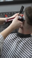 Professional barber grooming client's hair using electric clipper, delivering precise cut with...