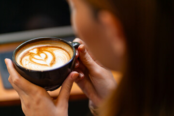Beautiful Asian woman sitting by the window in a cozy café, enjoying a latte and pastry while...