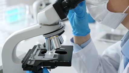 Scientific professional wearing blue protective gear examining microscope lens, performing detailed...