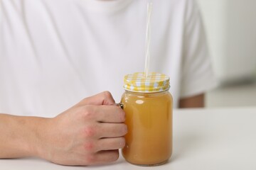 Man with mason jar of orange juice at white table indoors, closeup. Refreshing drink