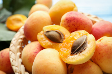 Many fresh apricots in wicker basket against blurred background, closeup